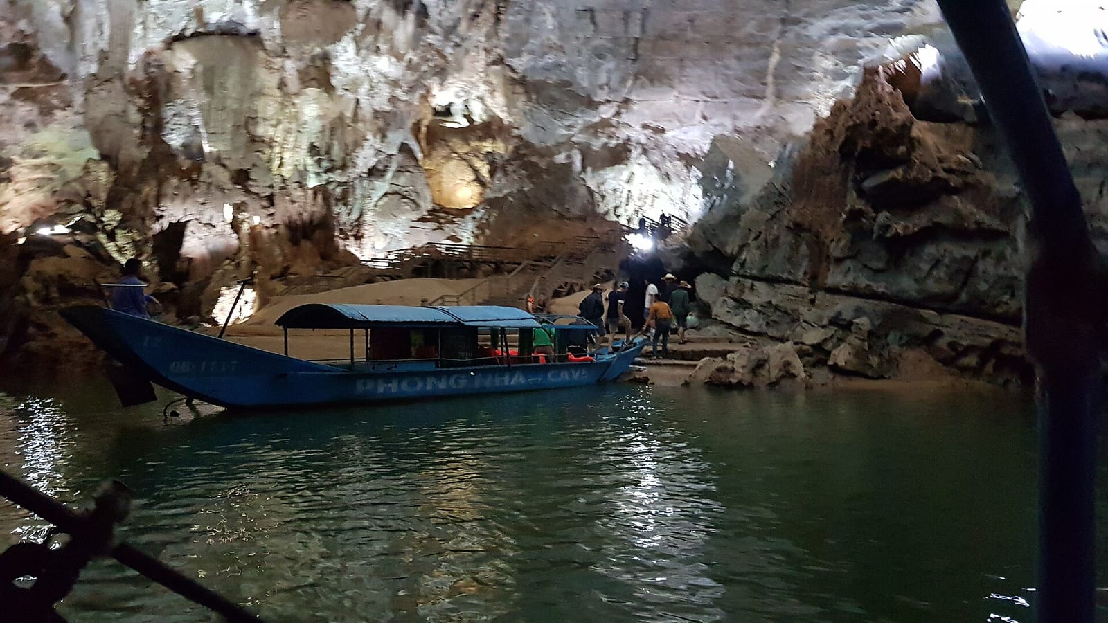 סירת תיירים עם הכיתוב PHONG NHA CAVE עוגנת בפתח המערה על הנהר